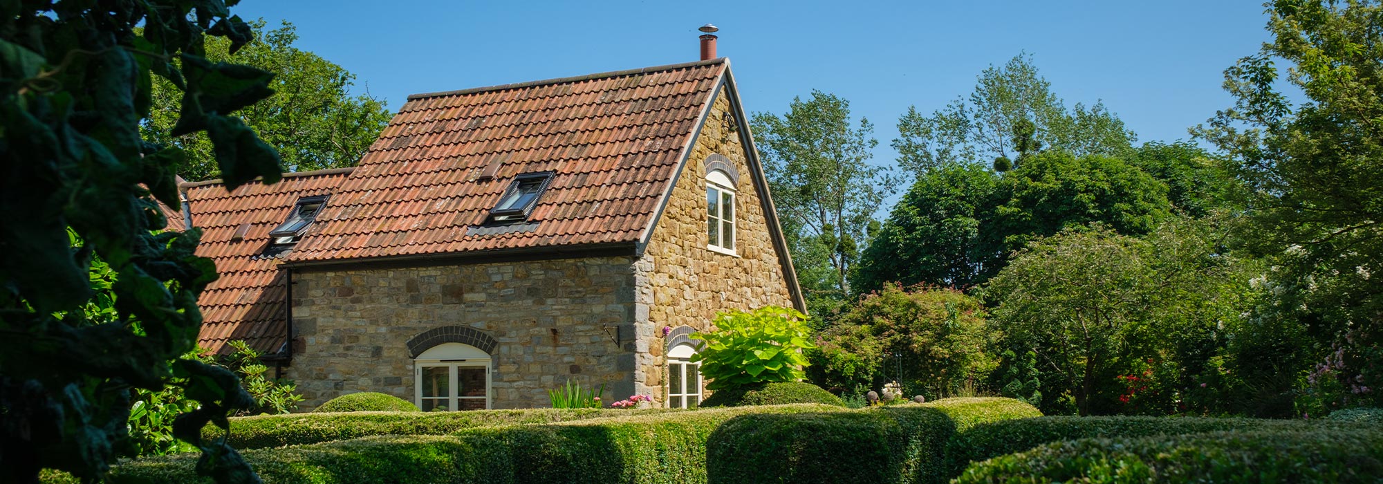 Picture of Pond Cottage surrounded by Hedges and other plants.