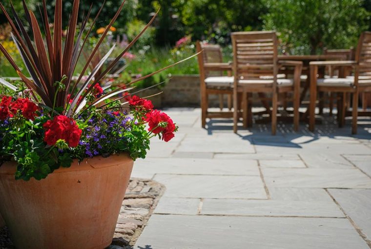 Patio, with red flowers in a plant pot and a table with chairs.